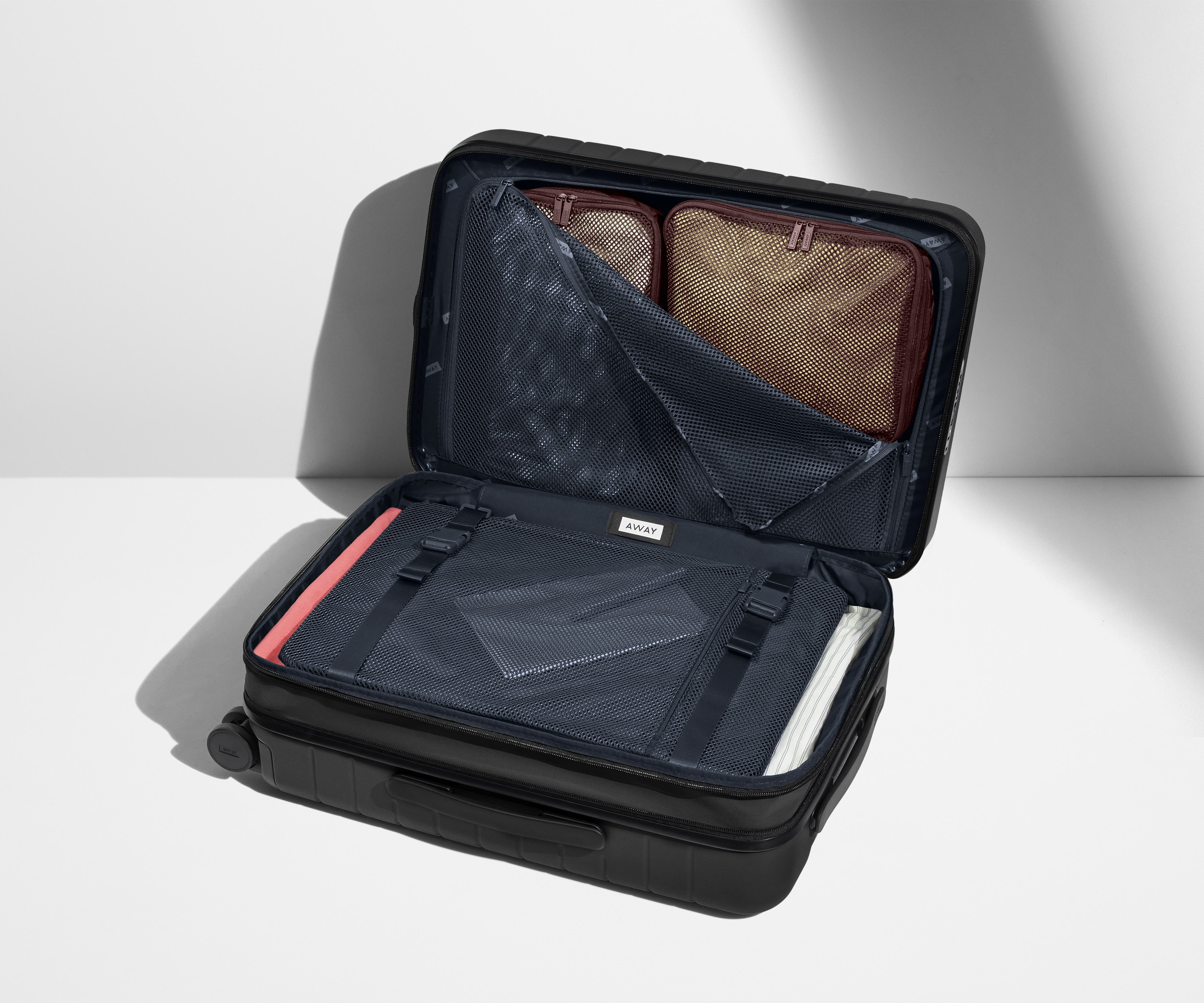 The Bigger Carry-On Flex suitcase in Jet Black shown open on its side and packed with Away's packing organizers to show capacity and the interior compression system, designed to help you pack more in