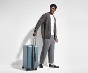 Male-presenting person standing next to a Medium Flex suitcase for scale