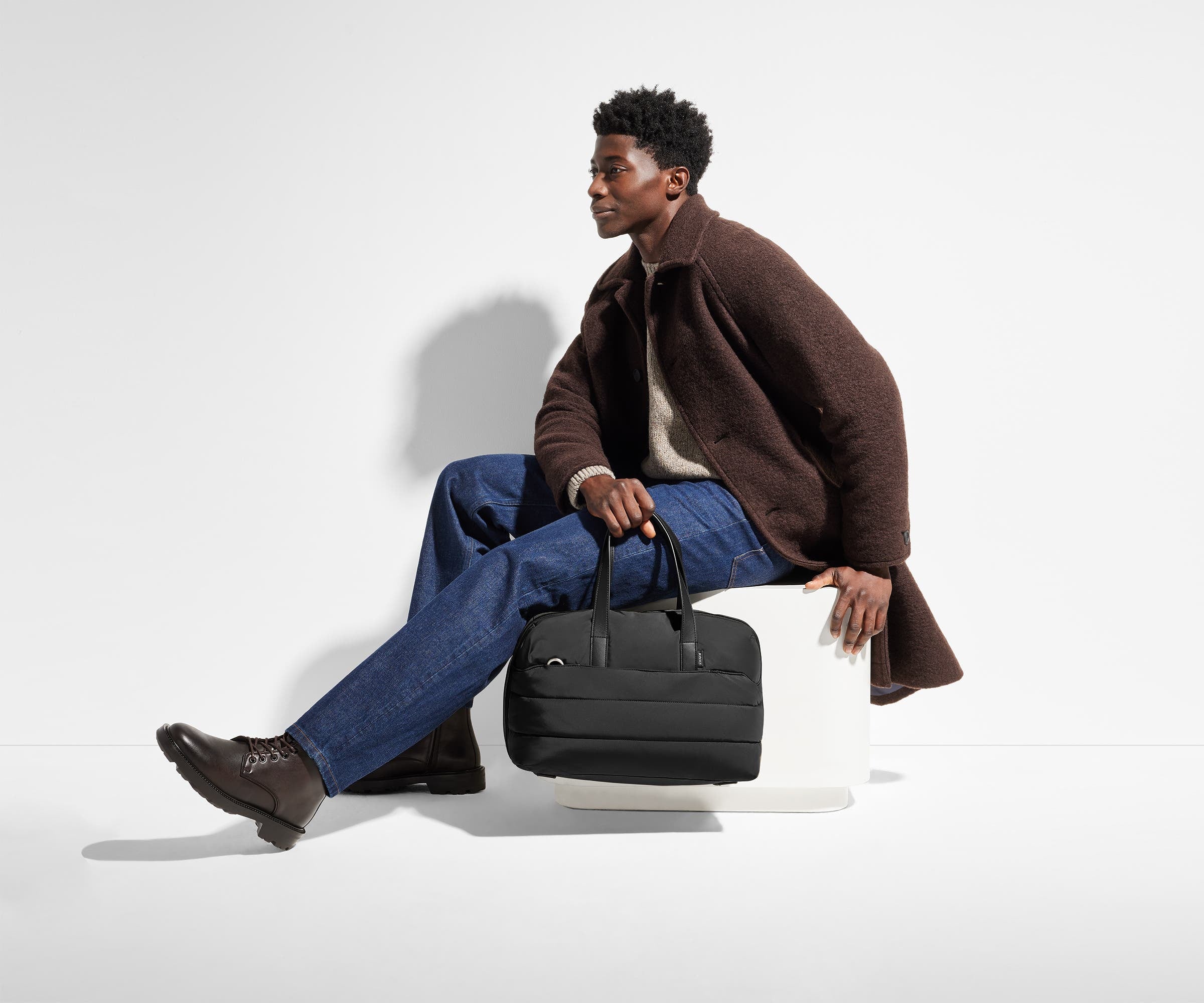 6'1" person holding the Quilted Everywhere Bag by its top leather handles while sitting down