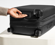 The Bigger Carry-On Flex suitcase in Jet Black shown from below highlighting the underside grab handle